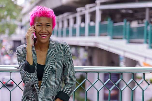 时髦年轻叛逆的亚洲女商人的肖像 粉红色的头发在城市户外的人行天桥上酷交谈朋克