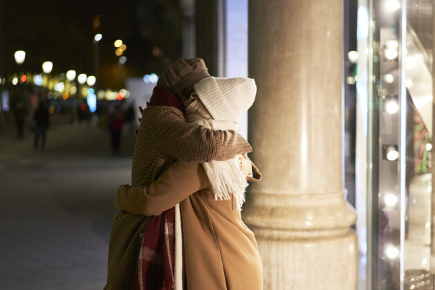 城市两个女人互致问候一起拥抱晚上在城里冬装照明冬天