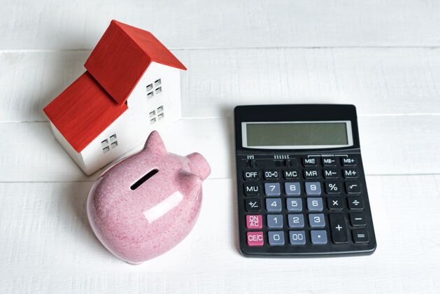 结构粉红色的猪存钱罐 计算器和面包板模型的房子有一个红色的屋顶上的灯背景.概念租房 买卖房地产计算器房地产金融