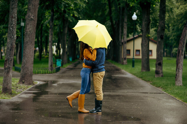 在一起情侣在公园接吻 夏天下雨戴曼雨中的女人站在雨伞下 漫步小径上的浪漫约会 小巷里的潮湿天气年轻森林人类
