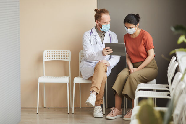 医学职业女病人坐在医院的走廊上 一边看数字平板电脑的显示器 一边向她展示治疗方法沟通实验服听诊器