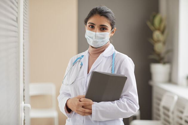 防护口罩戴着防护面具 穿着白大褂的女医生的画像 手里拿着医疗卡 看着医院的前面技术全科医生数字平板电脑