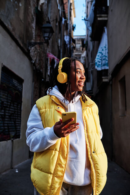 户外非洲裔美国妇女一边用手机一边用耳机听音乐户外.城市概念生活方式音乐非洲