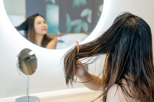 镜子特写镜头：悲伤的年轻女子用木梳子刷洗她在镜子前受损纠结的湿发发刷刷子拉