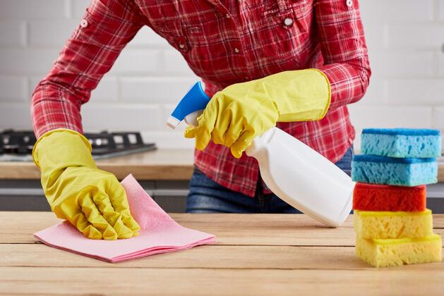 清洁戴着黄色防护手套的女人用白色瓶子喷雾 海绵和抹布清洁木桌海绵保护抛光