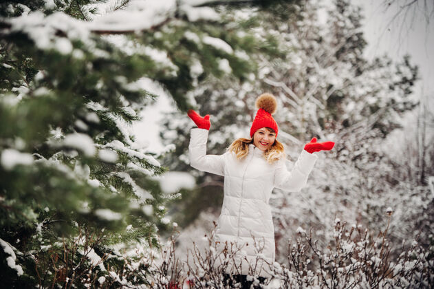 自然一个穿着白衣服 戴着红帽子的女人在寒冷的冬天的肖像森林女孩在冰雪覆盖的冬季森林里雪年轻红帽子