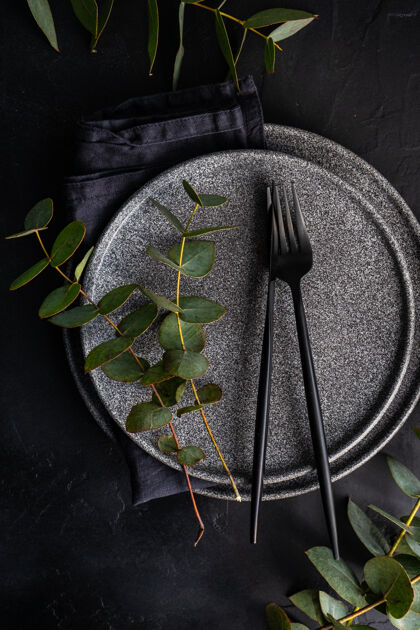 叶子黑色的石头器皿 黑色的餐具 放在用新鲜的绿色桉树叶装饰的黑色水泥桌上餐具自然餐桌