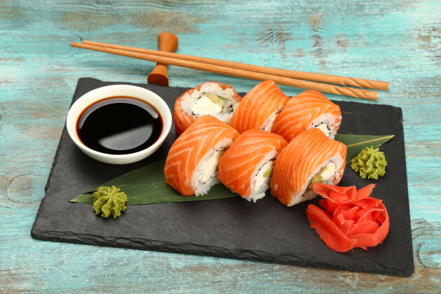 新鲜六个费城寿司卷的特写镜头 生鲑鱼放在蓝色桌子上的黑石板上 高角度观看生食物健康