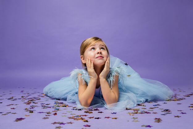 小一个小女孩躺在地板上 手里拿着五彩纸屑 抬头看着紫色乐趣肖像地板