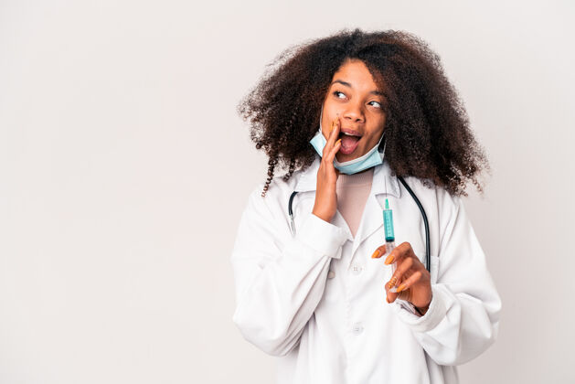耳语年轻的非洲裔美国卷发女医生手里拿着注射器正在说一个秘密的热门新闻 一边看非洲裔美国人针头诊所