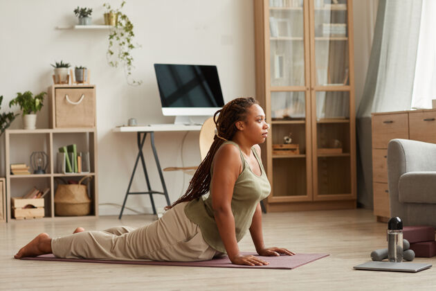 全身非洲年轻女子在客厅的运动垫上做伸展运动早晨身体意识瑜伽