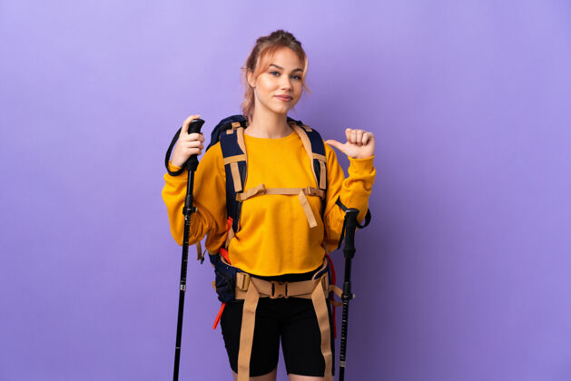 徒步旅行带着背包和登山竿的女孩在孤独的紫色上骄傲而自满表达女人冒险