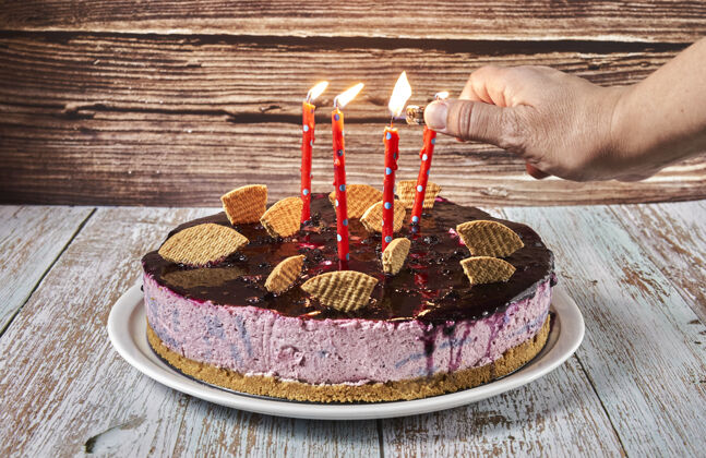食品一个女人的手在用饼干装饰的森林水果慕斯蛋糕上点燃蜡烛奶油巧克力蛋糕