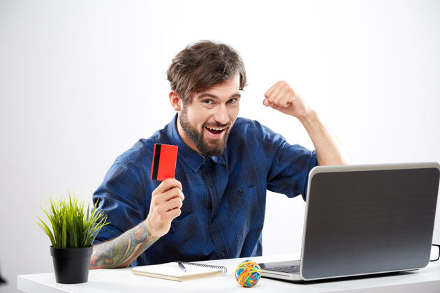 自由职业者帅哥穿着蓝色衬衫坐着拿着笔记本电脑 网购概念 写真 手机网购 拿着信用卡 兴高采烈男性男人网上购物