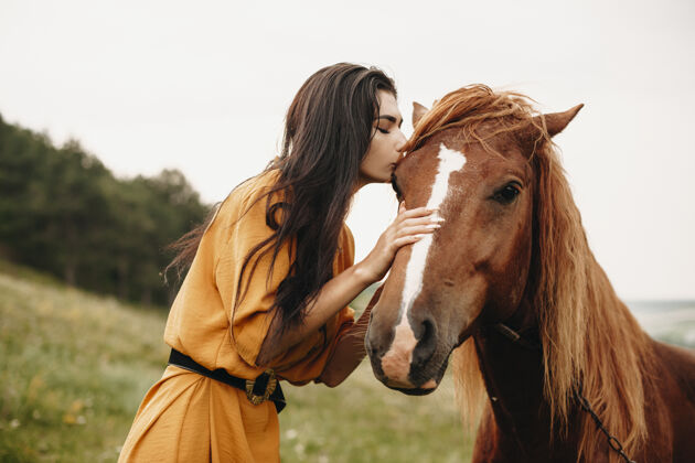 头发一个迷人的年轻女孩在田野上亲吻一匹马的户外镜头波西米亚波西米亚领域