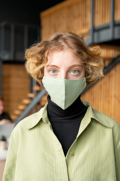 成人年轻的金发上班族穿着休闲服 戴着防护面具 站在楼梯口的摄像机前看着你们流感病毒恐惧外科口罩