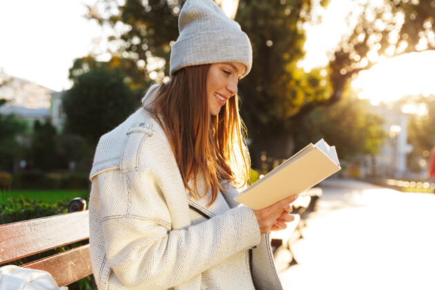 移动一个红发女人坐在户外的长凳上拿着一本书抱着女人年轻