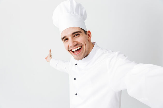 电话穿着制服的快乐厨师长孤立地站在白墙上 自拍男人餐厅厨师