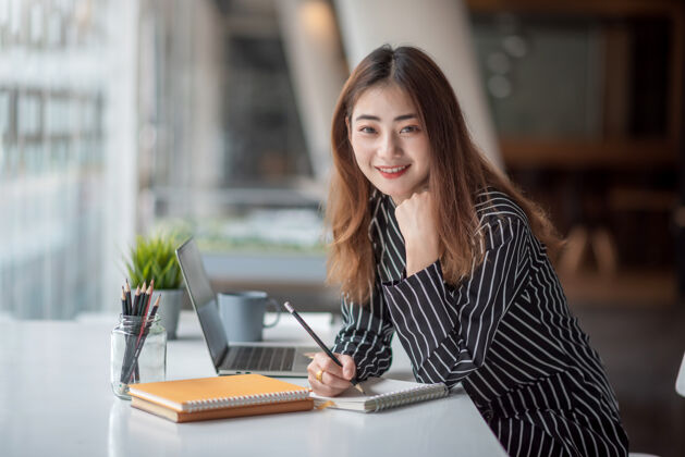 商务女性年轻的亚洲女商人的画像美丽迷人的微笑坐在办公室工作办公室看对着镜头职业经理好看