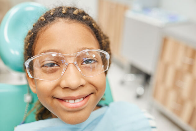 室内戴着护目镜的小女孩坐在牙医的椅子上微笑的特写镜头护目镜快乐实验室