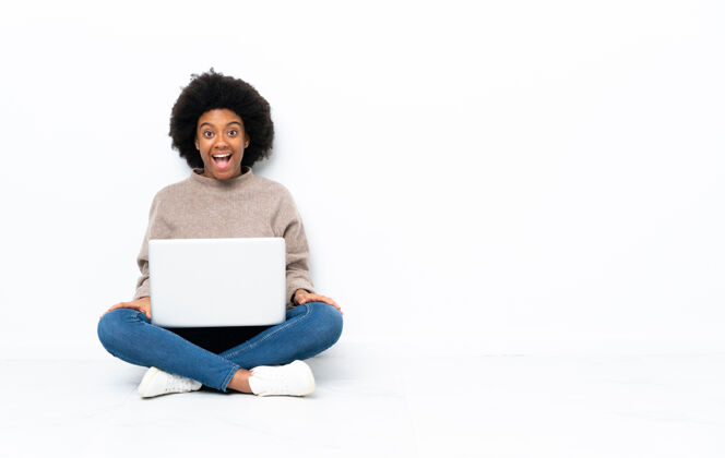美丽年轻的非洲裔美国妇女拿着笔记本电脑坐在地板上 脸上露出惊讶的表情尴尬电脑害怕