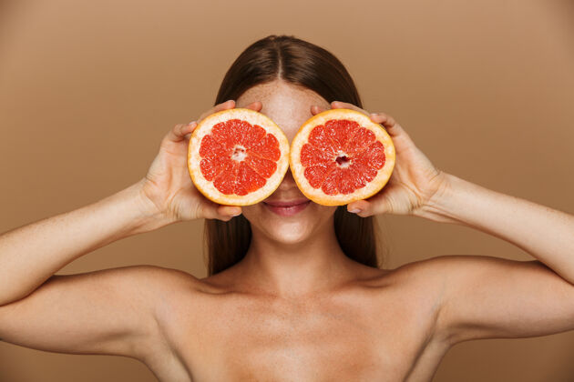 维生素美丽的肖像 一个美丽健康的年轻裸体女子长着红色的头发显示切片柚子隔离在米色墙上女人姿势姜