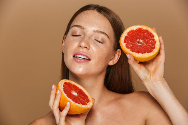 饮食美丽的肖像 一个美丽健康的年轻裸体女子长着红色的头发显示切片柚子隔离在米色墙上感性纯洁一半