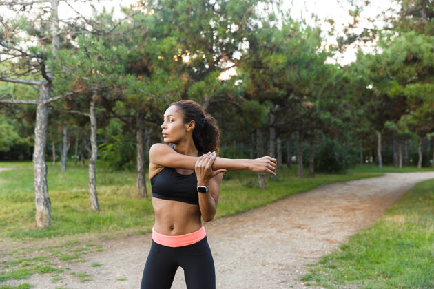 早晨美丽的非洲裔美国妇女20多岁穿着黑色运动服做运动 并伸展她的身体在绿色公园非洲运动成人