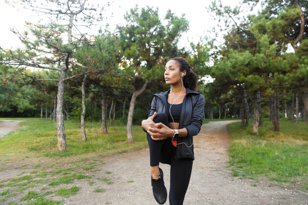 女性美丽的非洲裔美国妇女20多岁穿着黑色运动服做运动 并伸展她的身体在绿色公园成人吸引力保健