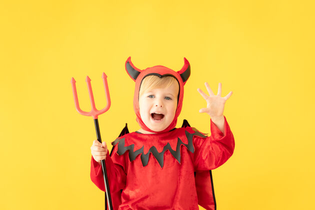 大笑滑稽的孩子穿着魔鬼服装对着黄色的表面恐怖季节恐怖