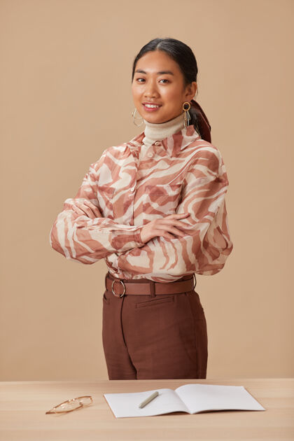 室内亚洲年轻教师双臂交叉站在桌旁 微笑着站在前面的画像办公桌办公室商务女性
