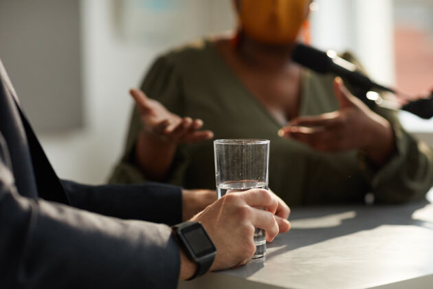 人手特写镜头的男子坐在桌边与一杯水在商业面试的女人饮水杯商务办公室