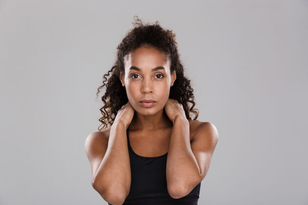 年轻人一位自信的美国黑人女运动员站在灰色的墙上活跃训练身体