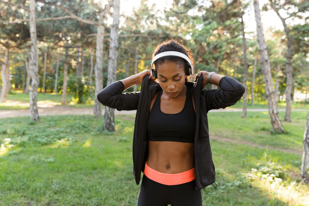 耳机20多岁的美女穿着黑色运动服 戴着耳机 穿过绿色公园健身成人美国