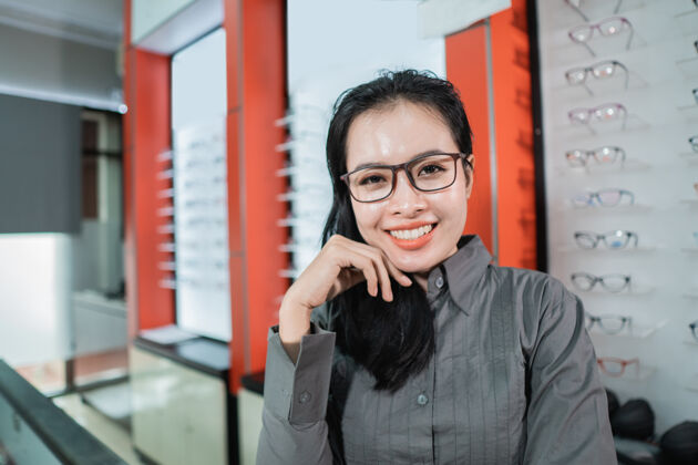 顾客一个美丽的微笑的女人戴着眼镜 背景是眼镜店的眼镜陈列架客户人穿着