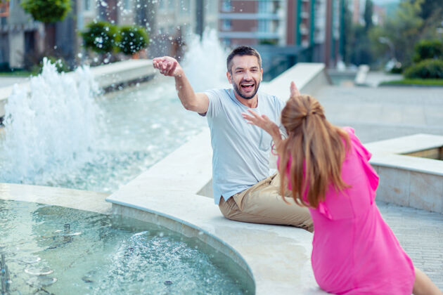 男朋友快乐的时光快乐的夫妇坐在一起 在喷泉边享受快乐支持乐趣感情