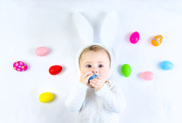 欢呼宝宝穿得像兔子 在白色的表面上放复活节彩蛋童年微笑手
