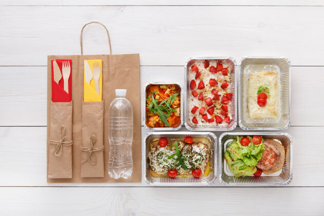 餐具健康食品配送 日常膳食和零食营养 蔬菜 肉类 水瓶和水果在锡箔盒和牛皮纸包装俯视图 平放在白色木材与复印空间沙拉平铺纸
