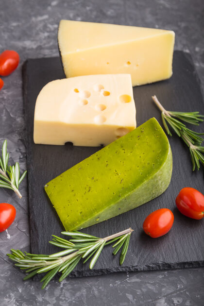 布里绿色罗勒奶酪和各种奶酪与迷迭香和西红柿在黑色板岩板上的黑色混凝土表面小吃烹饪草药