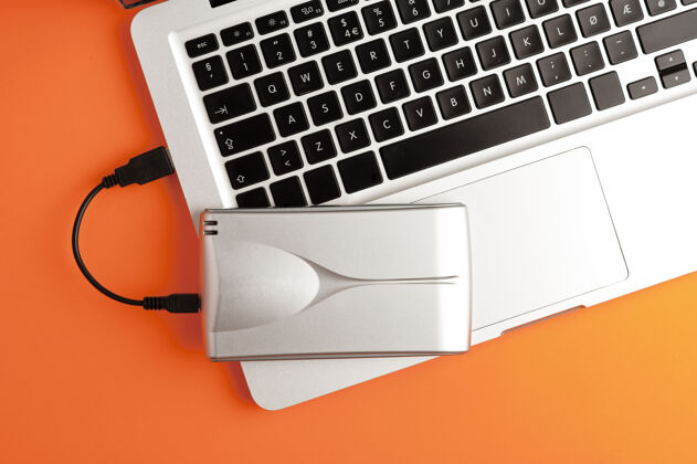 屏幕铝制外置硬盘放在笔记本电脑的顶部橙色背景 俯视图电脑外部硬