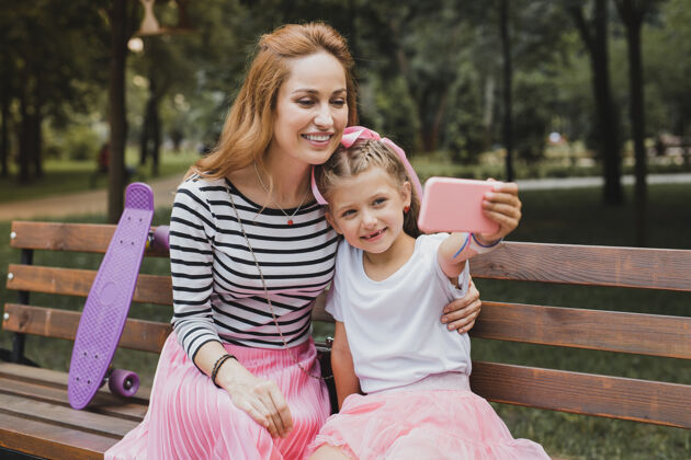 露天自拍现代可爱的微笑女孩和她美丽的母亲一起自拍公园放松感情