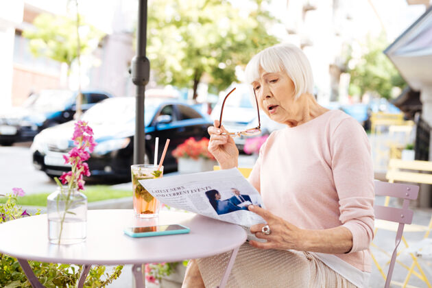 老年人突发新闻惊讶的老妇人拿着眼镜看报纸自信积极进步