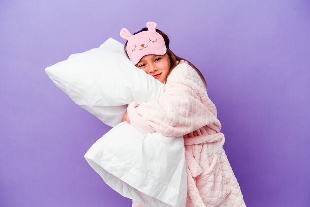 孩子气小女孩抱着一个枕头快乐地孤立在紫色上早晨拥抱孩子