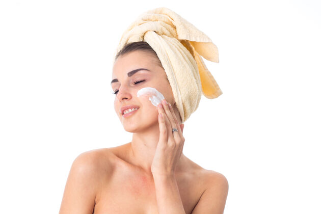 女性年轻漂亮的女人用毛巾在头上涂上隔离在白墙上的护肤霜皮肤应用特写