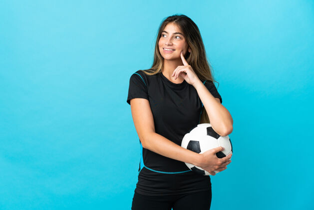 球一个年轻的足球运动员 一个被隔离在蓝色墙上的女人 一边抬头一边思考着一个想法年轻人女人休闲