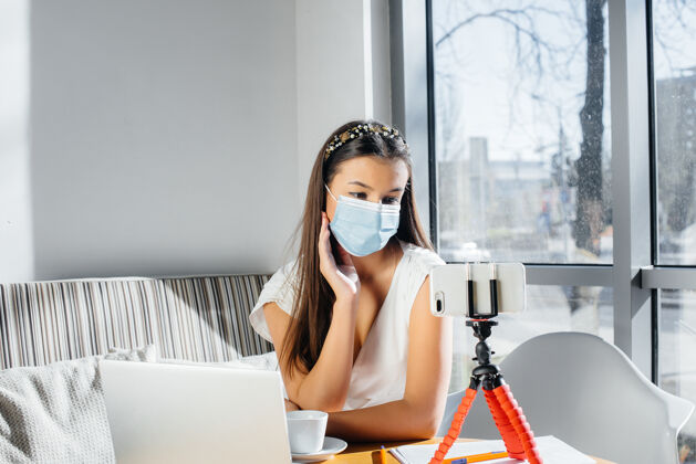 流感一个小女孩戴着面具坐在一家咖啡馆里 带着一个视频博客对着镜头交流感染女性大流行