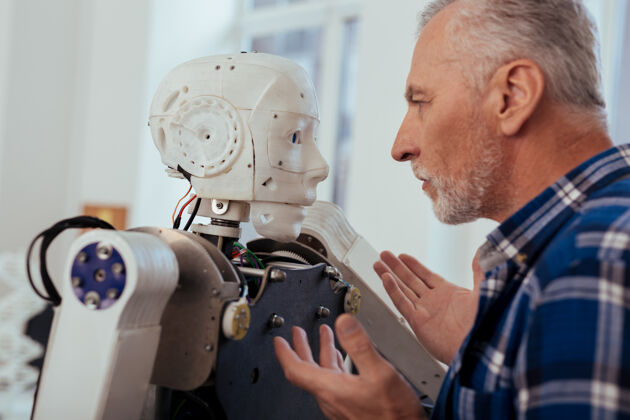 医疗保健先进的技术严肃的智能工程师站在机器人面前看着他成熟机器人老年人