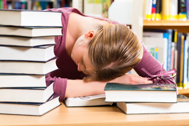 年轻学生—年轻女子在图书馆看书学习 她睡着了 又累又累大学学术过度工作