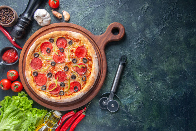 木板美味的自制比萨饼放在木制砧板上西红柿大蒜番茄酱绿色包油瓶在黑暗的表面右侧西红柿比萨饼晚餐