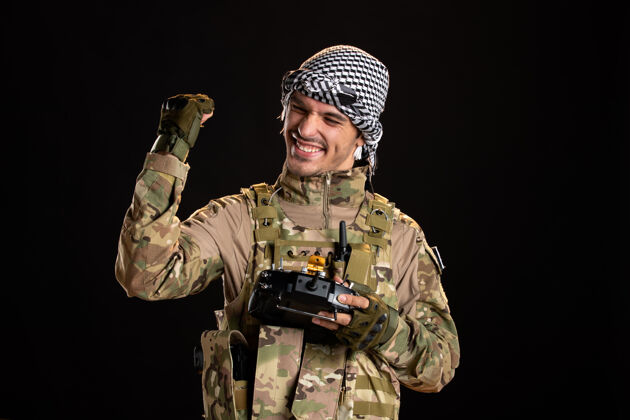 军队快乐的巴勒斯坦士兵在黑墙上用遥控器遥控器军服使用